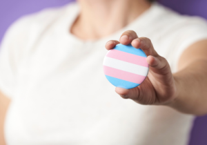 Image of person holding a blue, pink and white transgender badge